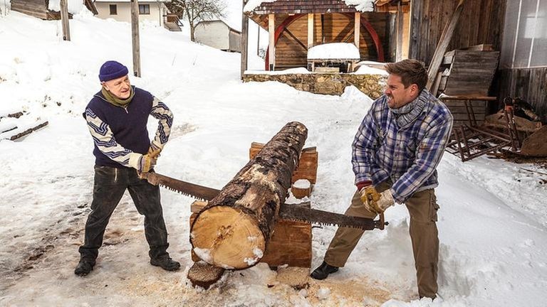 Toni und Andreas sägen einen Baumstamm durch, es liegt Schnee