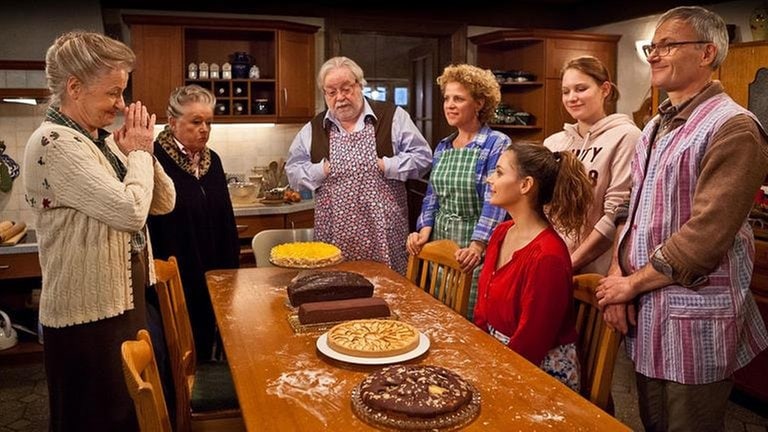 Die Familie hat sich um den Küchentisch versammelt, auf dem mehrere frisch gebackene Kuchen stehen