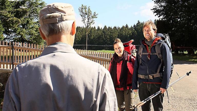 Karl, den man von hinten sieht, trifft vor dem Hof auf zwei Wanderer