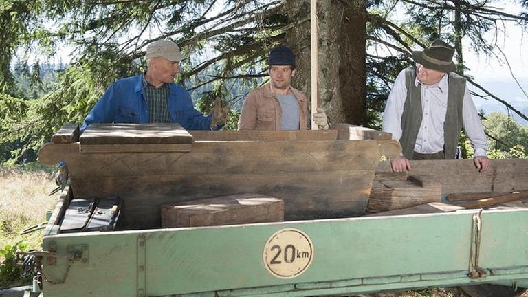 Karl, Riedle und Zimmermann stehen an einem Anhänger, auf dem ein Trog aus Holz steht