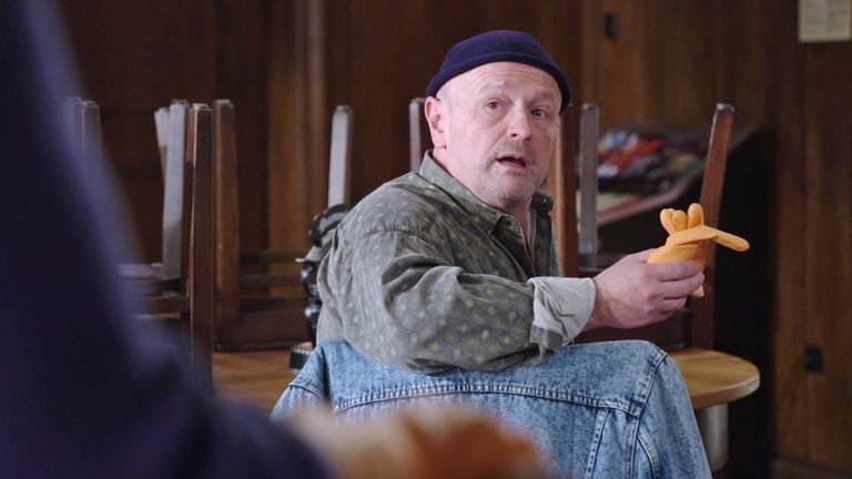 Toni sitzt am Stammtisch und hat Putzhandschuhe in der Hand