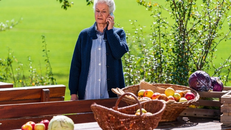 Johanna steht hinterm Fallerhof und hält ihr Handy ans Ohr.