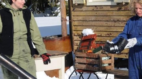 Rosi und Bea reinigen vor Rosis Bauwagen im Schnee ein Ofenrohr