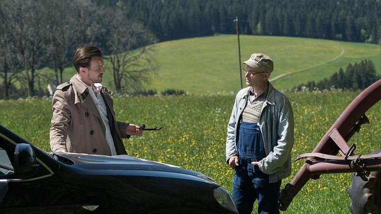 Constantin und Heinz unterhalten sich auf der Wiese, davor Constantins Limousine, daneben Karls Traktor