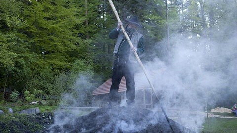 Toni steht auf dem dampfenden Kohlenmeiler und bearbeitet ihn mit einer langen Holzstange