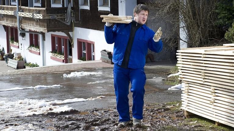 Matthias Steiner trägt mehrere dicke Holzbretter auf der Schulter