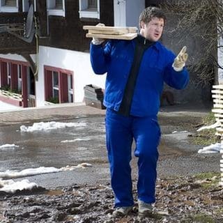 Matthias Steiner trägt mehrere dicke Holzbretter auf der Schulter