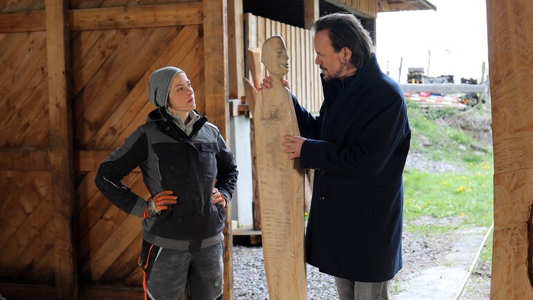 Sophie und Constantin stehen mit Sophies Holzskulptur am Eingang des Sägewerks