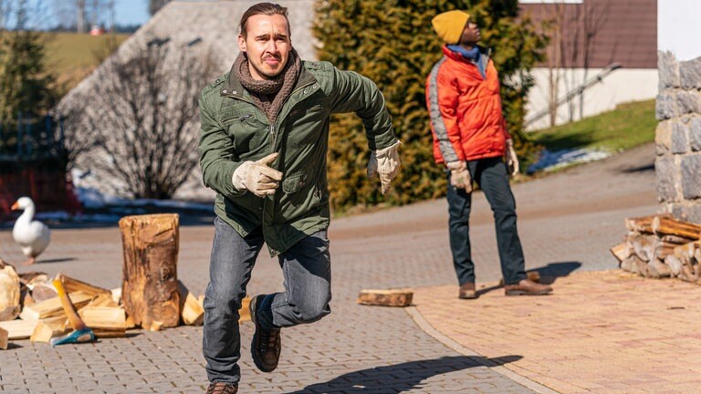 Sebastian rennt vom Hackklotz weg, Tayo blickt am Hof hoch