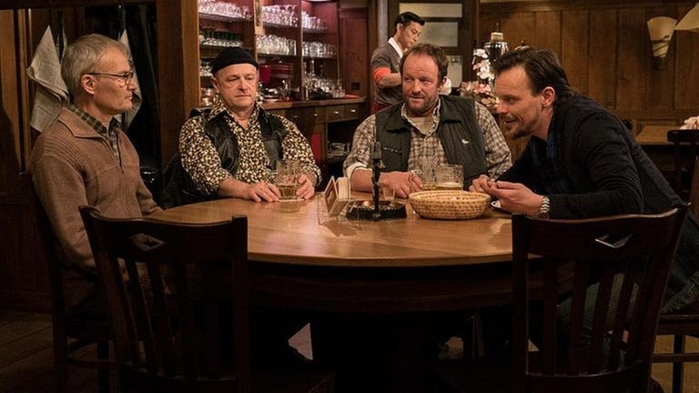 Karl, Toni, Bernd und Constantin am Stammtisch. Im Hintergrund sieht man Tu, wie er Bier zapft.