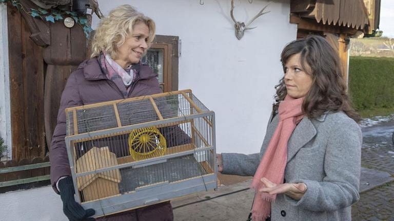 Kati, die einen Hamsterkäfig hält, und Eva stehen vor dem Leibgedinghaus