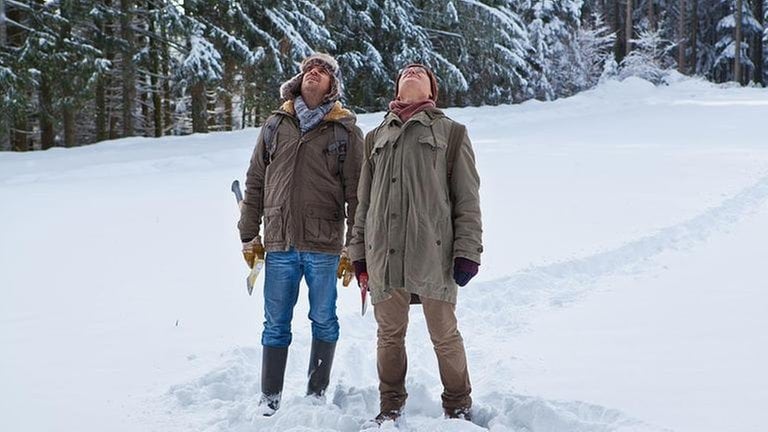 Andreas und Karl stehen im tiefen Schnee am Waldrand und schauen in den Himmel