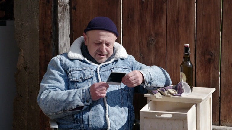 Toni sitzt vor einer Scheune und sieht sich ein Polaroid-Foto an