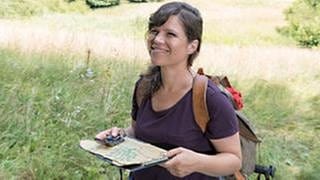 Eva auf einer blühenden Wiese, in der Hand eine Wanderkarte