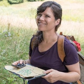 Eva auf einer blühenden Wiese, in der Hand eine Wanderkarte