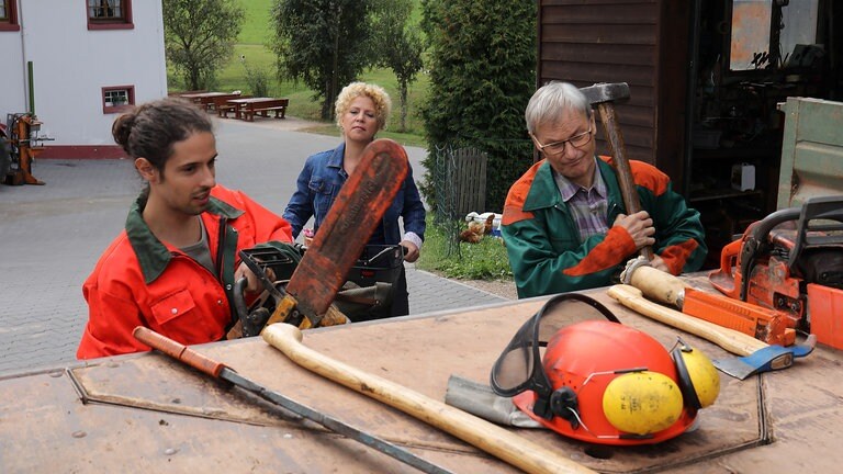 Karl und Albert richten ihr Werkzeug für die Waldarbeit, Bea im Hintergrund