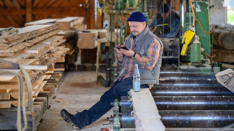 Toni sitzt im Sägewerk und tippt auf seinem Handy