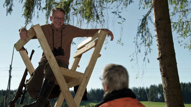 Bernhard sitzt auf einem von Karls transportablen Hochsitzen und guckt auf Karl, den man nur von hinten sieht