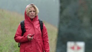 Bea wandert im Regen, sie trägt ein rotes Regencape