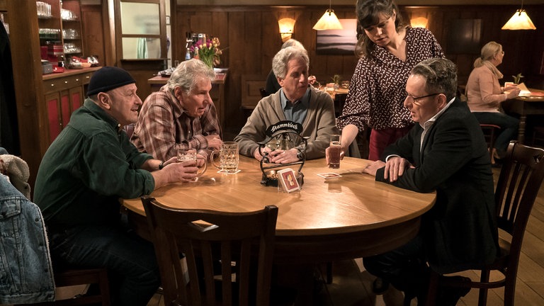 Bernhard mit Schorsch, Toni und Leo am Stammtisch, Eva bringt ihm ein Mineralwasser. 