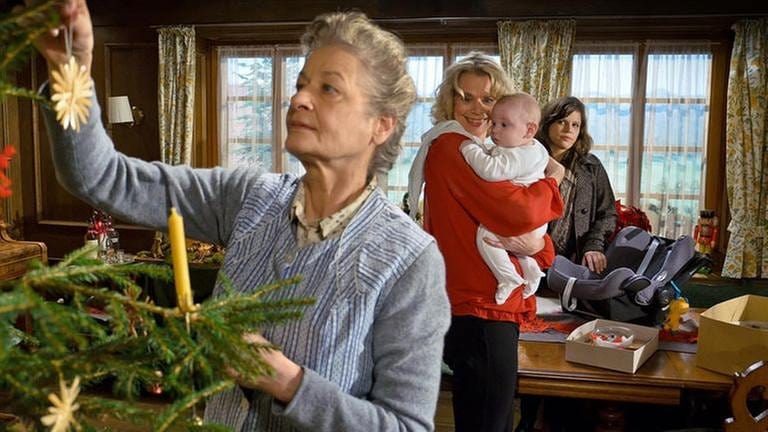 Johanna schmückt den Weihnachtsbaum, im Hintergrund hält Kati ihre Enkelin Carlotta, Eva guckt skeptisch