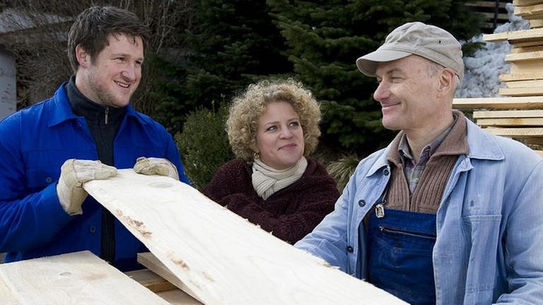 Matthias Steiner, Bea und Karl hinter einem hohen Bretterstapel