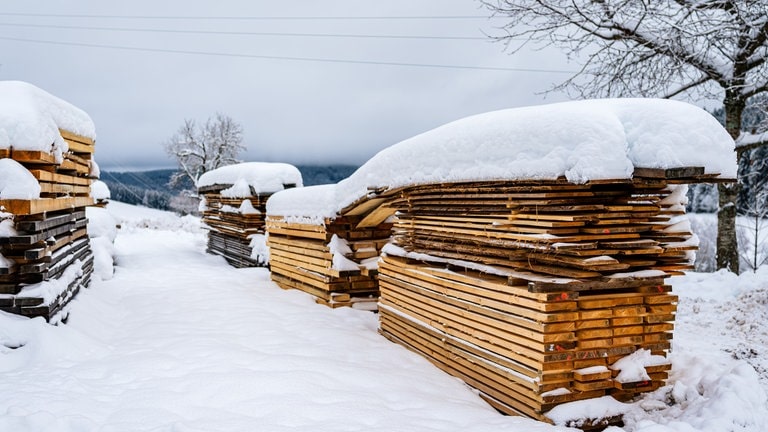 Verschneite Holzstapel vor dem Sägewerk