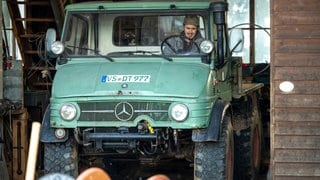 Sebastian (Dominik Stricker) sitzt in seinem grünen Unimog, der in der Traktorscheune steht