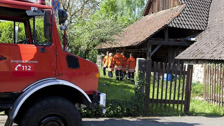 Im Vordergrund ein Feuerwehrauto, dahinter der Feuerwehrtrupp im Einsatz