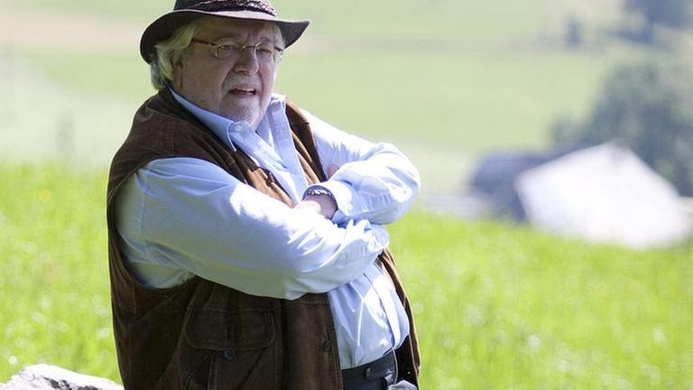 Hermann Faller sitzt auf einem Baumstamm, der auf der Sommerwiese hinterm Fallerhof liegt