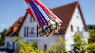 Ein Bündel mit Umhüllungen für Glasfaserkabel hängt an einem Schild und vor einem Wohnhaus. 