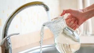 Eine Frau füllt einen Krug mit Wasser aus einem Wasserhahn.