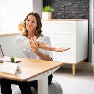 Frau sitzt am Schreibtisch und macht eine Fitnessübung