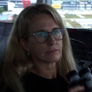 Fluglotsin Carola End sitzt mit einem Fernglas in der Hand im Tower des Flughafens Stuttgart