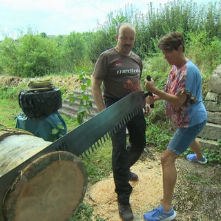 Markus Dengler, der Macher des Holzfällerwettbewerbs in Widdern sägt gemeinsam mit der Landesschau-Reporterin Sonja an einem Baumstamm.