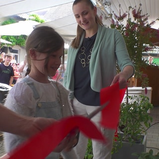 Das kleine Mädchen Carolin eröffnet den Hofladen, indem sie das rote Bänchen mit der Schere teilt.