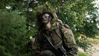 Rekrut steht bei einer Heimatschutz-Übung in Bundeswehr-Uniform im Wald