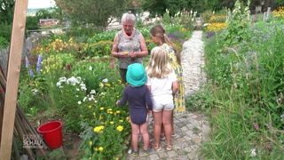 Maria Tittor zeigt Kindern in einem Garten eine Blume