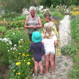 Maria Tittor zeigt Kindern in einem Garten eine Blume