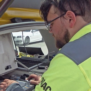 ADAC Pannenhelfer Bastian Morgenstern steht an seinem Auto vom Pannendienst und wertet technische Daten aus.