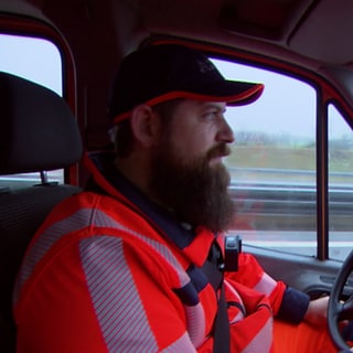 Der Autobahnstreckenwart sitzt im Auto und fährt in roter Warnweste. 