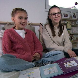 Nele Cuypers und Jule Gärtner aus Weikersheim haben ein Kinderbuch für die Herzenssache geschrieben. Sie sitzen mit dem Buch auf dem Bett.