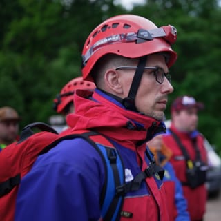 Ein Bergretter mit Helm und Licht steht in einer Gruppe von anderen Bergrettern und hört zu