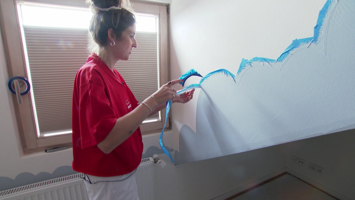 Eine junge Frau zieht Klebeband von einer Wand, auf die eine blaue Wolke gemalt wurde