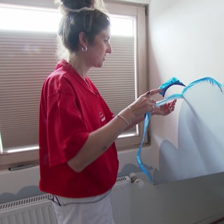 Eine junge Frau zieht Klebeband von einer Wand, auf die eine blaue Wolke gemalt wurde 