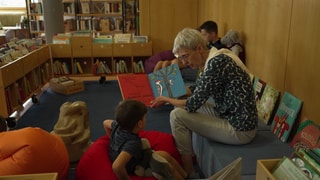 Eine ältere Frau zeigt einem kleinen Jungen ein Buch. 