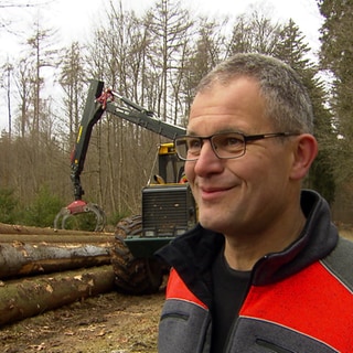 Mann steht im Wald. Holzernetmaschine im Hintergrund