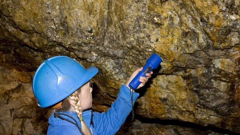 Kind entdeckt mit Taschenlampe Mineralien an den Wänden eines Bergwerkes