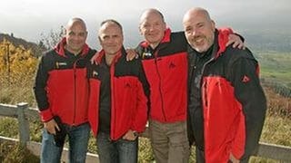 Die Wetterreporter Michael Kögel, Harry Röhrle, Michael Kost und Thomas Miltner stehen nebeneinander, umarmen sich und lächeln in die Kamera.