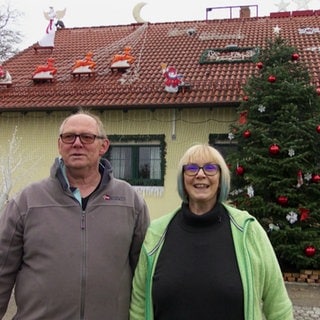 Ehepaar steht vor weihnachtlich geschmücktem Haus